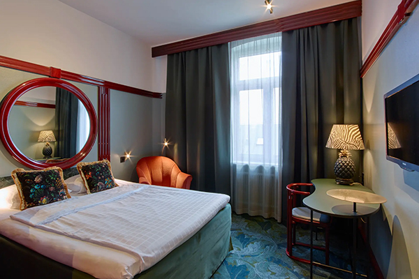 Hotellrum med en fint bäddad säng. Kulörta kuddar på sängen. Mörkblå fondvägg bakom med en svartvit tavla.