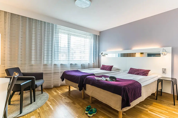 Hotellrum med en fint bäddad säng. Kulörta kuddar på sängen. Mörkblå fondvägg bakom med en svartvit tavla.