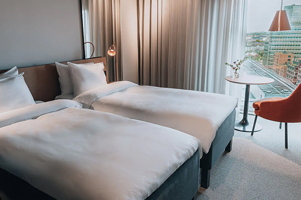 Hotellrum med en fint bäddad säng. Kulörta kuddar på sängen. Mörkblå fondvägg bakom med en svartvit tavla.