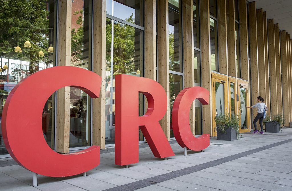 En bartender dekorerar tre cocktails i stora vinglas med is och limeklyftor på en bardisk. Dryckerna har en rödaktig färg och serveras i en livlig bar- eller restaurangmiljö.