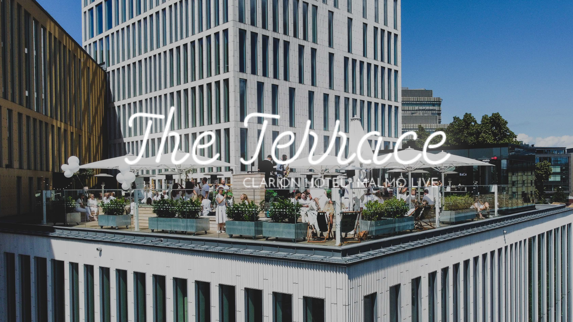 The Terrace, Clarion Hotel Malmö Live En bartender dekorerar tre cocktails i stora vinglas med is och limeklyftor på en bardisk. Dryckerna har en rödaktig färg och serveras i en livlig bar- eller restaurangmiljö.